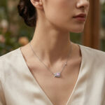 Delicate silver pendant necklace with a pink gemstone surrounded by a diamond-studded flower on a cream blouse.