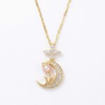 Gold necklace with a diamond-encrusted crescent moon pendant and a pink pearl flower, topped by a diamond cross on a gold chain.